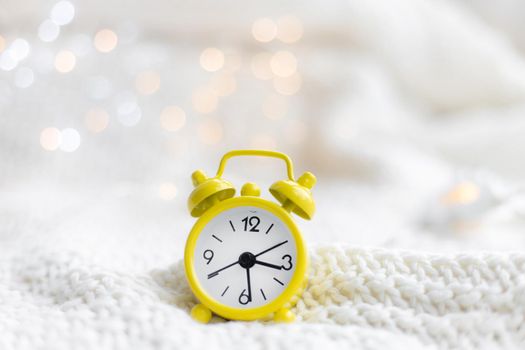 Alarm clock on a plaid with a garland . Yellow alarm clock. Cozy vibes . Home comfort. New Year and Christmas. Decorating
