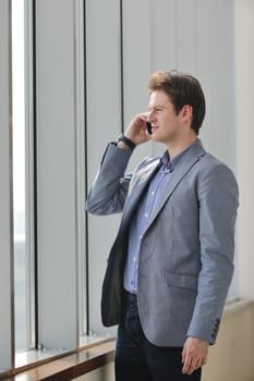 young business man talk by cellphone over bright window in big hall