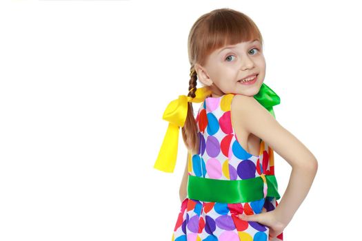 A sweet little blonde girl with long pigtails, in which large colored bows are braided, and a short bangs on her head. In a short summer dress, a pattern of multi-colored circles.