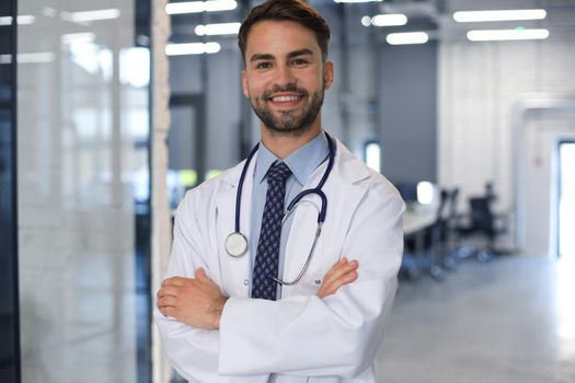 Handsome friendly young doctor on hospital corridor looking at camera, smiling