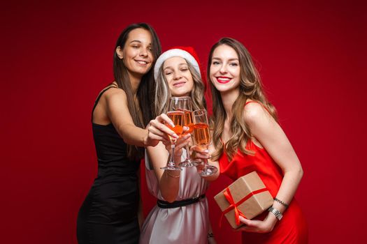 Happy young women friends with gift and champagne celebrating holiday together on party on red background, copy space. High quality photo