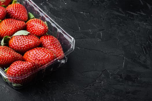 Red ripe strawberrie in clear plastic tray, on black background with copy space for text