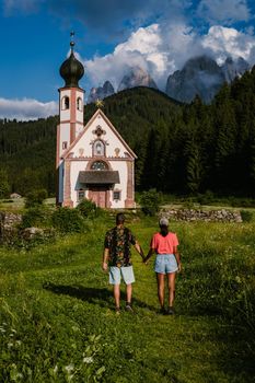 Santa Maddalena church village in front of the Geisler, Val di Funes, Italy, Europe. couple mid age man and woman on vacation in Italy, Asian woman, caucasian man, Alpine church Ranui, Santa Maddalena