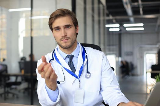 Smiling handsome male doctor talking at camera with patient