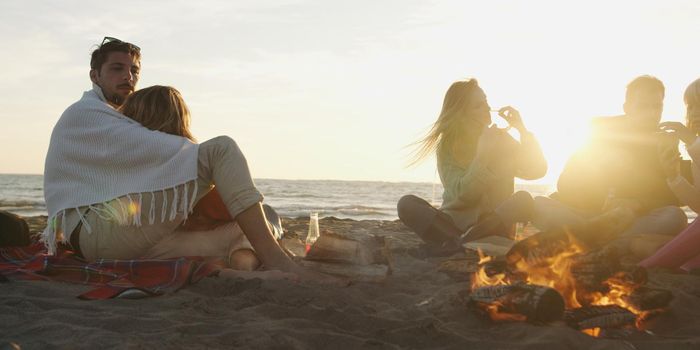 Young Couple Relaxing By The Fire, Drinking A Beer Or A Drink From The Bottle.