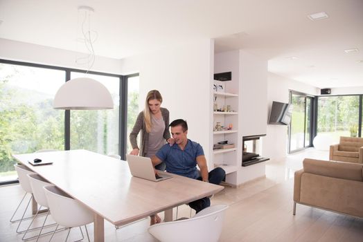 Young couple using laptop computer at luxury home together, looking at screen, smiling.