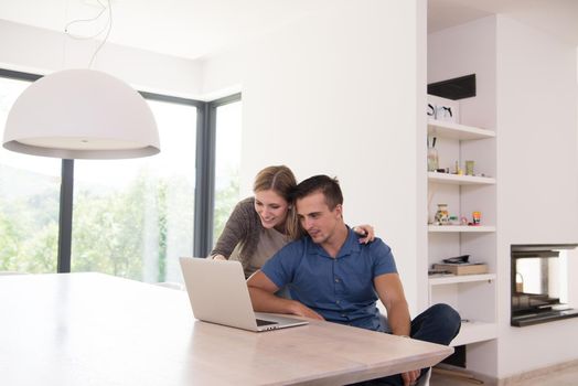 Young couple using laptop computer at luxury home together, looking at screen, smiling.