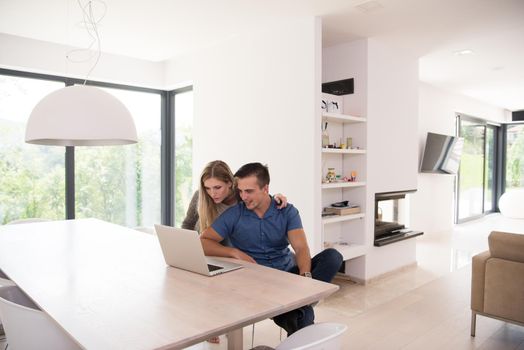 Young couple using laptop computer at luxury home together, looking at screen, smiling.