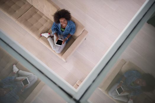 Young african american woman at home relaxing in her luxury lliving room reading a digital tablet PC surf internet and work top view