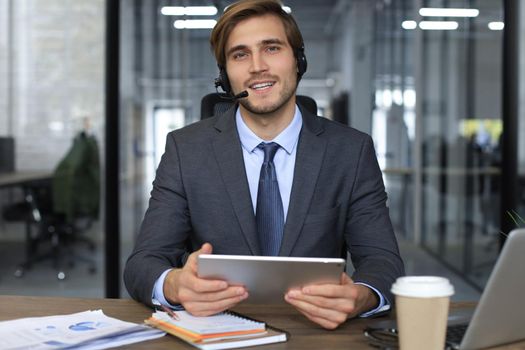 Cheerful young support phone male operator in headset, at workplace while using laptop, help service and client consulting call center concept.