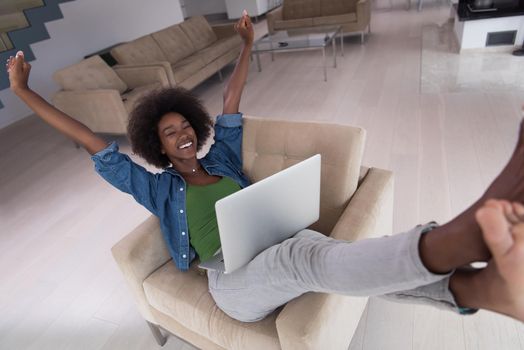 Young african american woman at home in the chair relaxing in her luxury lliving room reading  laptop PC surf internet and work