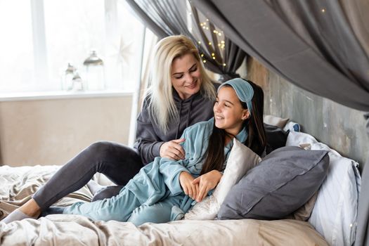 Mother and daughter are lying on bed in pajamas and talking about something. Family time.