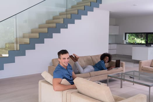 Young multiethnic couple relaxes in the luxury living room, using a tablet and laptop computer