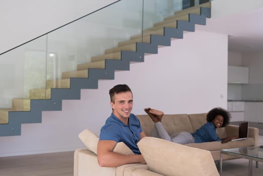 Young multiethnic couple relaxes in the luxury living room, using a tablet and laptop computer