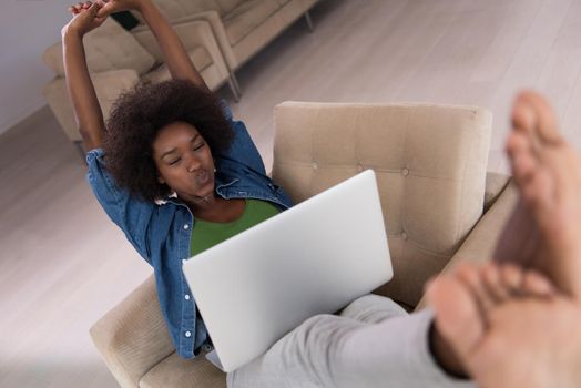 Young african american woman at home in the chair relaxing in her luxury lliving room reading  laptop PC surf internet and work