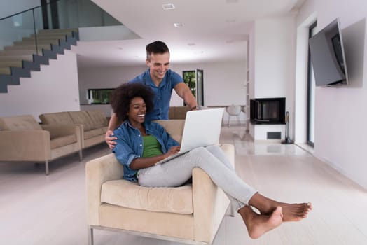 Young multiethnic couple sitting on an armchair in the luxury living room, using a laptop computer