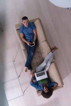 Young multiethnic couple relaxes in the luxury living room, using a tablet and laptop computer top view