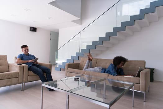 Young multiethnic couple relaxes in the luxury living room, using a tablet and laptop computer