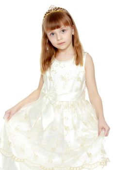 Beautiful little blonde girl with long blond hair and a short bangs. In a white ball dress.The girl is holding the edges of the dress with her hands.