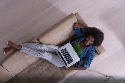 Smiling young African American woman using laptop while relaxing on sofa at luxury home top view