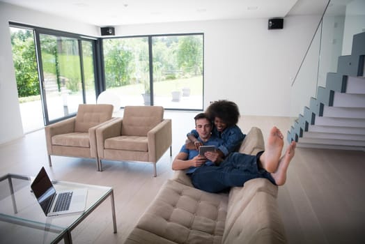 Young multiethnic couple relaxes in the luxury living room, using a tablet and laptop computer