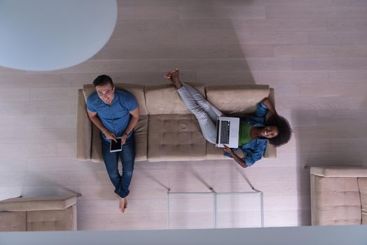 Young multiethnic couple relaxes in the luxury living room, using a tablet and laptop computer top view