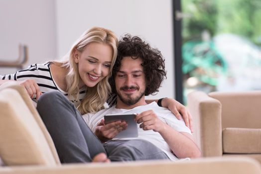 Young couple relaxing at luxurious home with tablet computers reading in the living room on the sofa couch.