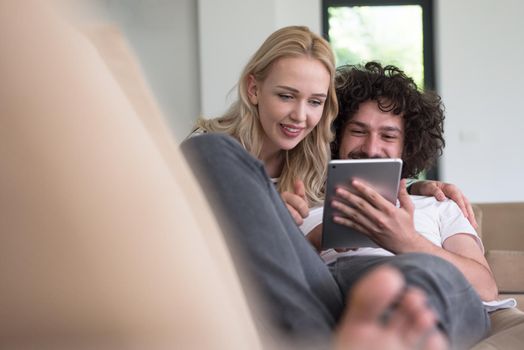 Young couple relaxing at luxurious home with tablet computers reading in the living room on the sofa couch.