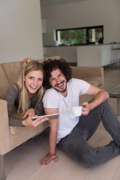 Young couple relaxing at luxurious home with tablet computers reading in the living room on the sofa couch.