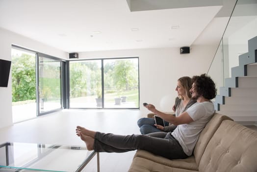 Young couple relaxes on the sofa in the luxury living room, using a tablet and remote control