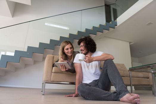 Young couple relaxing at luxurious home with tablet computers reading in the living room on the sofa couch.