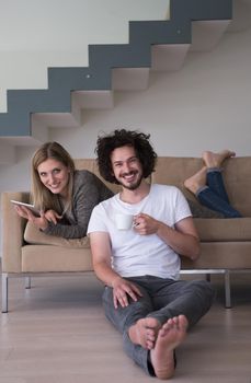 Young couple relaxing at luxurious home with tablet computers reading in the living room on the sofa couch.