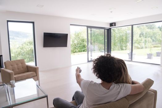 Rear view of couple watching television in living room their luxury home