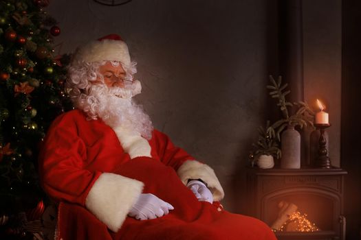 Santa Claus having a rest in a comfortable chair near the fireplace at home