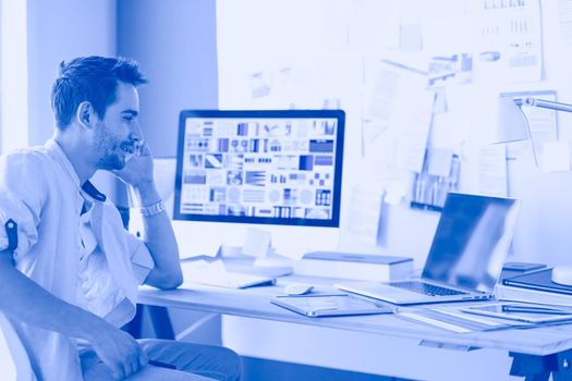 Portrait of young designer sitting at graphic studio in front of laptop and computer while working online