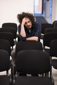 A student sits alone in a empty seats in a classroom