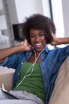 young beautiful African American woman enjoys listening to music with headphones and tablet in your armchair in her luxury home