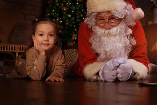 Santa Claus and child laying on floor at home. Christmas gift. Family holiday concept