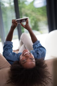 Young african american woman at home relaxing in her luxury lliving room reading a digital tablet PC surf internet and work