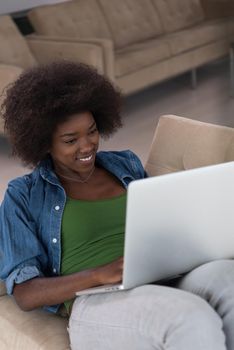 Young african american woman at home in the chair relaxing in her luxury lliving room reading  laptop PC surf internet and work