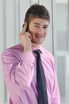 young business man talk by cellphone over bright window in big hall 