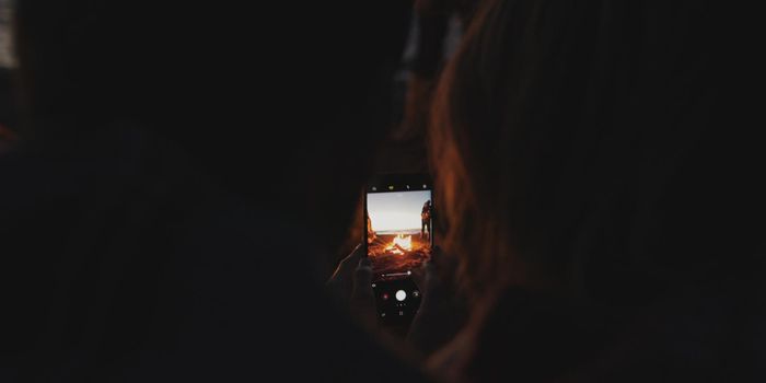 Boy Shows Girl A Picture On His Phone beside campfire on beach