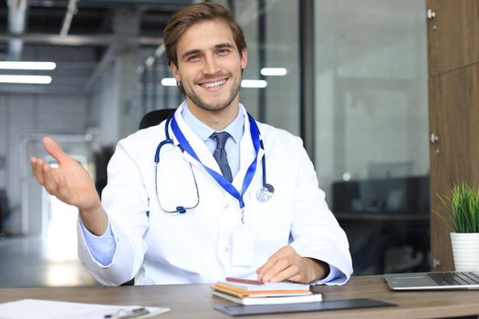 Smiling handsome male doctor talking at camera with patient