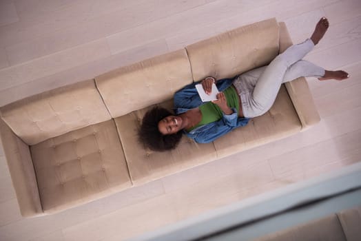 Young african american woman at home relaxing in her luxury lliving room reading a digital tablet PC surf internet and work top view