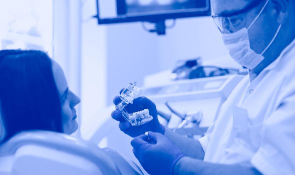 Senior male dentist in dental office talking with female patient and preparing for treatment.