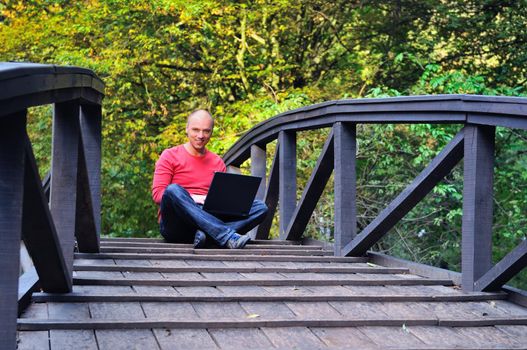 one young businessman working on laptop outdoor at wooden bridge  with green nature in background