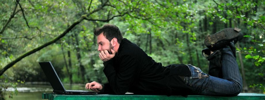 one young businessman working on laptop outdoor with green nature in background