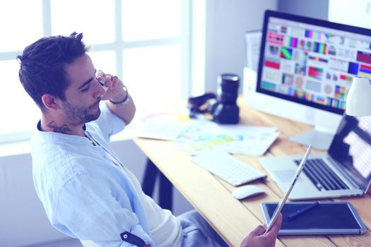 Portrait of young designer sitting at graphic studio in front of laptop and computer while working online