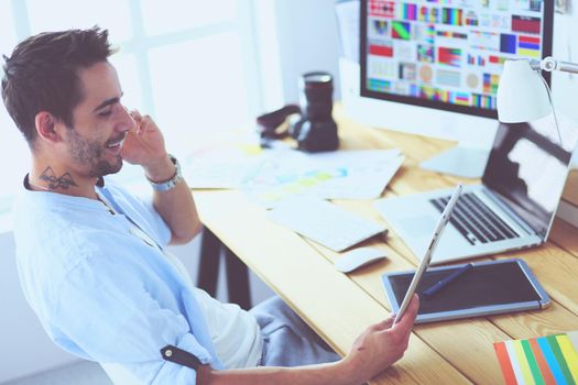 Portrait of young designer sitting at graphic studio in front of laptop and computer while working online