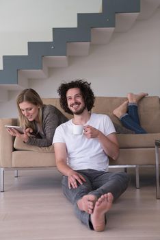 Young couple relaxing at luxurious home with tablet computers reading in the living room on the sofa couch.